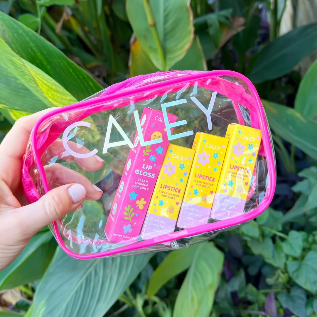 Hand holding Caley Cosmetics Clean and Cute Lip Kit with lipstick and lip gloss against green leaves.