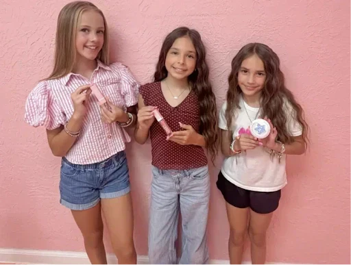 Three smiling girls holding Caley Cosmetics makeup products, celebrating fun and age-appropriate first makeup moments.