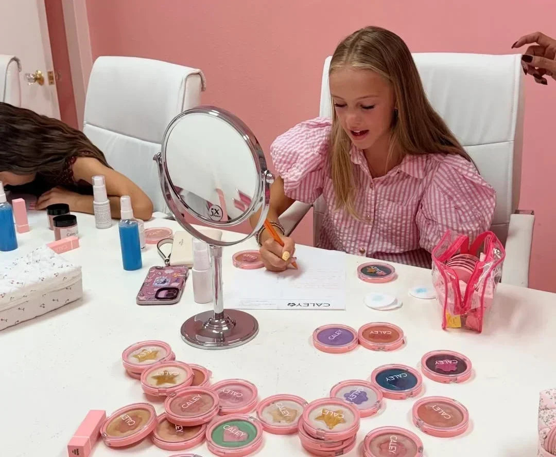 Child enjoying a creative makeup activity with Caley Cosmetics products and colorful beauty palettes on a table.