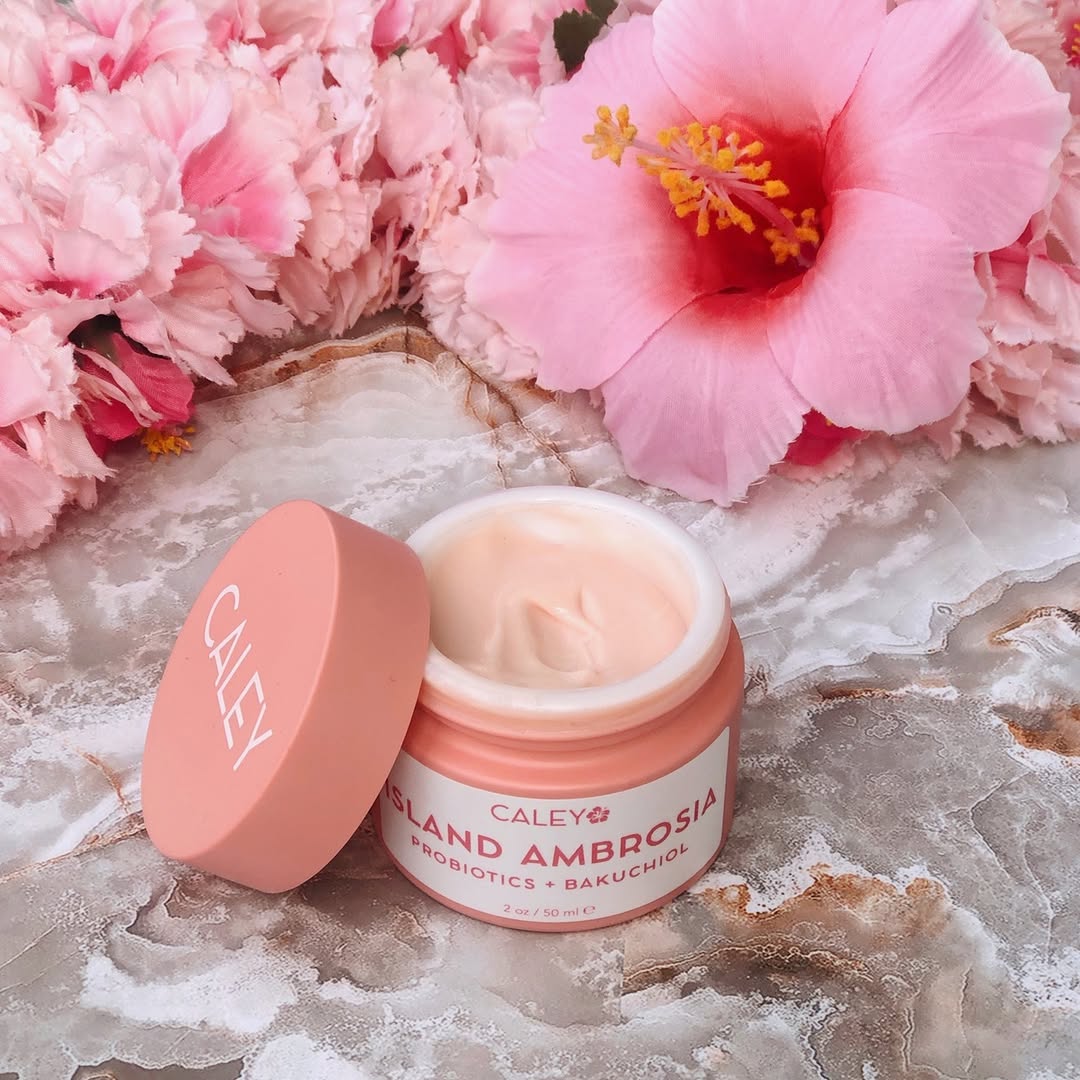 Caley Island Ambrosia probiotic moisturizer open beside pink hibiscus flowers