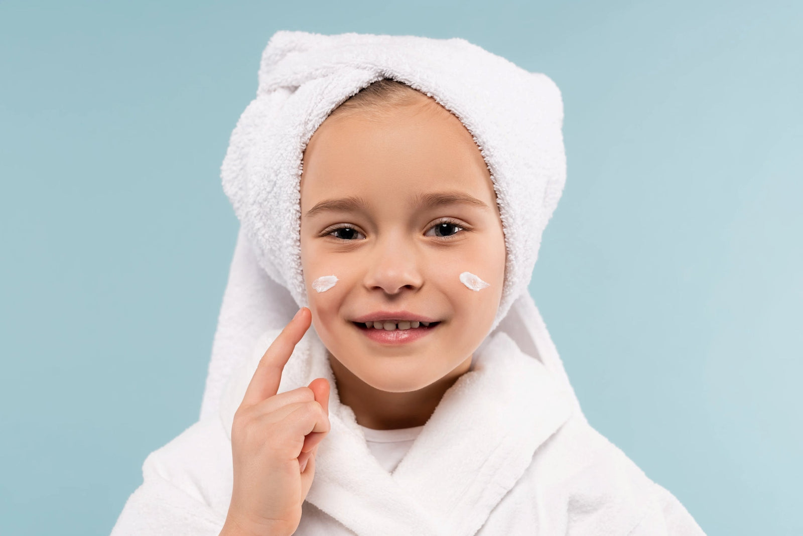 A girl applying moisturizer as part of a gentle skincare routine with a towel wrapped around her hair.