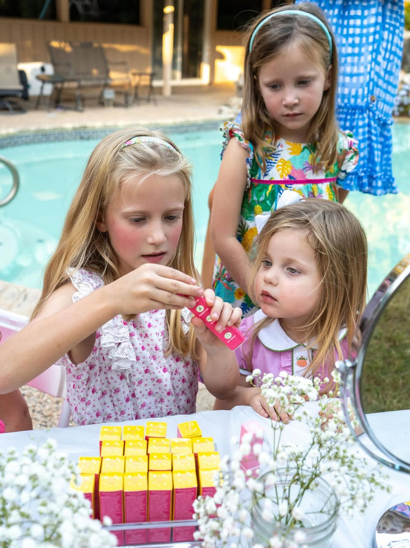 Girls testing Caley Cosmetics lipsticks at an outdoor table by the pool.