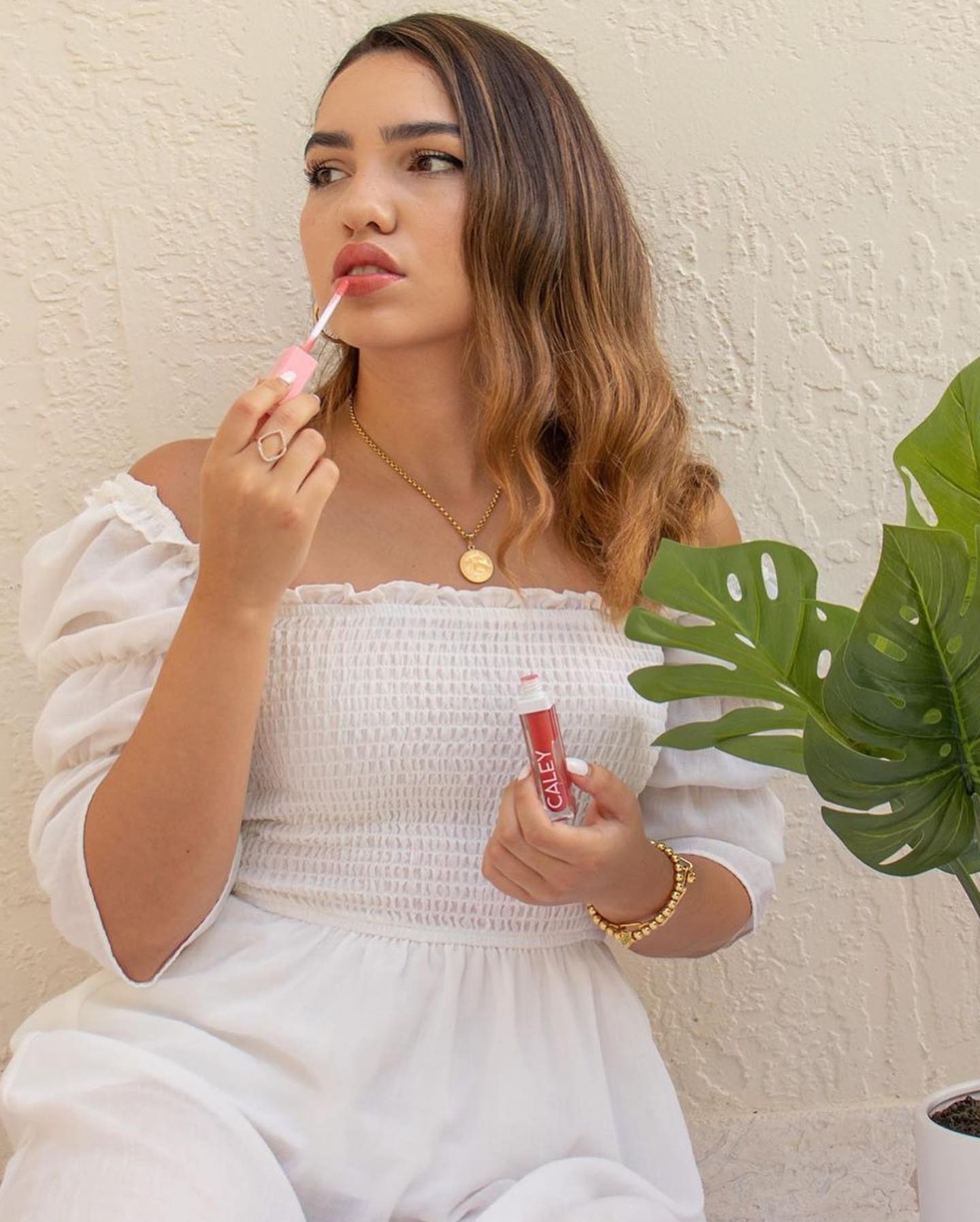 Caley Cosmetics lip stain being applied by a woman in a white dress, showcasing a soft, natural glow.