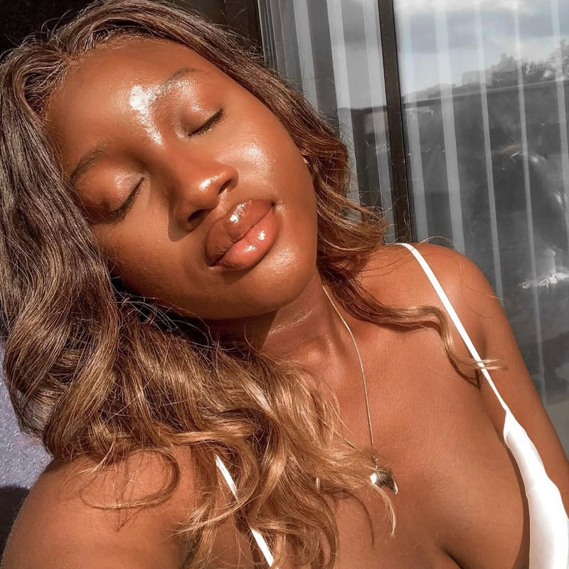 Woman with radiant skin and glossy lips enjoying natural sunlight, showcasing a fresh and dewy summer beauty look.