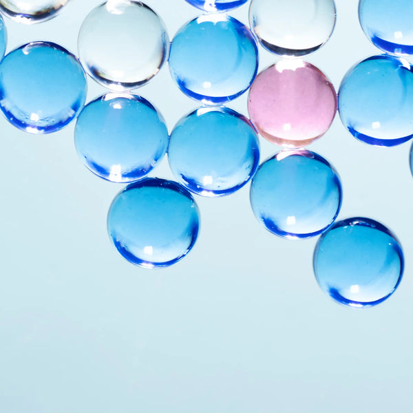 Clear blue glass marbles with a pink marble on a light blue background